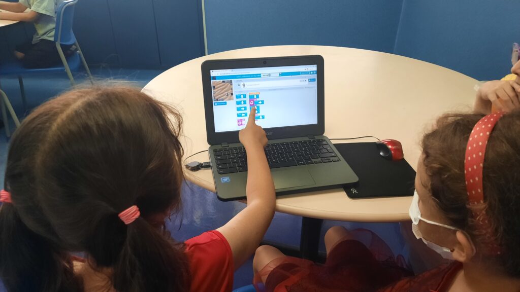 Duas crianças programando em blocos no computador, em aula da DHEL